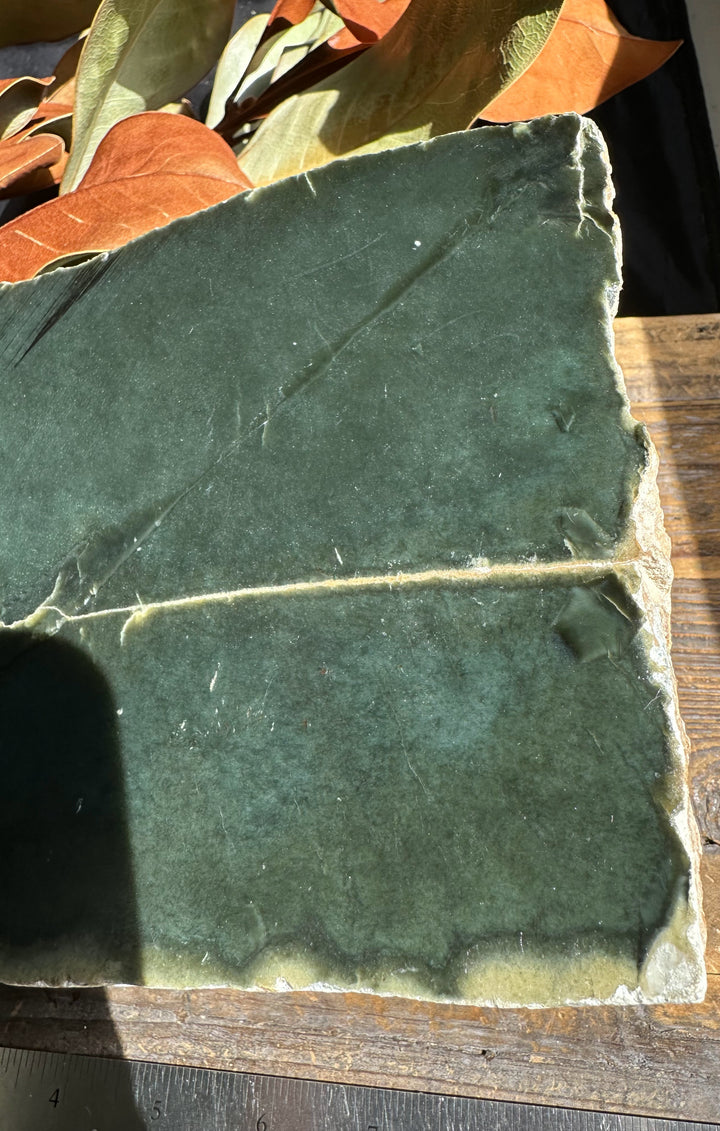 Wyoming Jade slab with dark green surface and rough edges on a wooden table