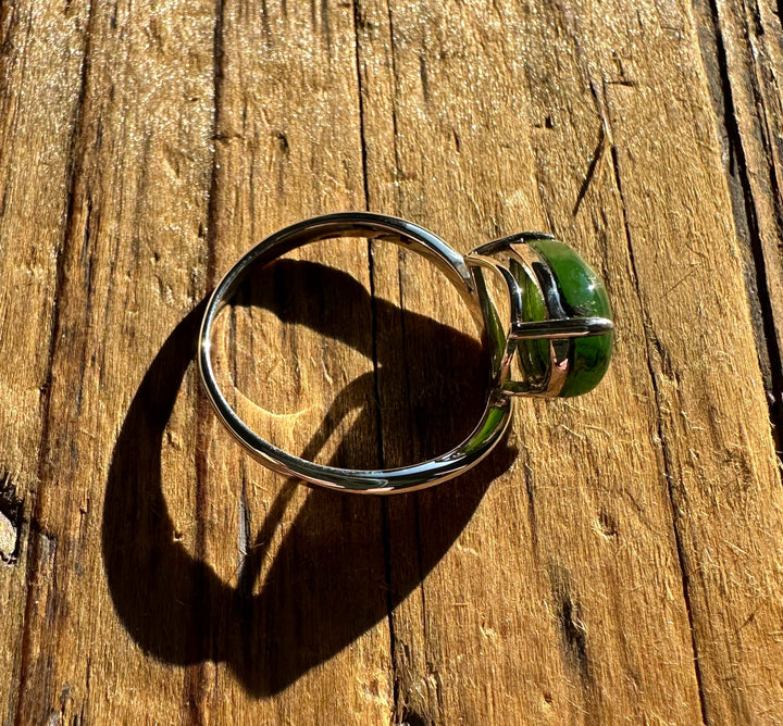 Canadian Jade and Silver Ring with a green jade centerpiece set in a silver band photographed on a wooden surface