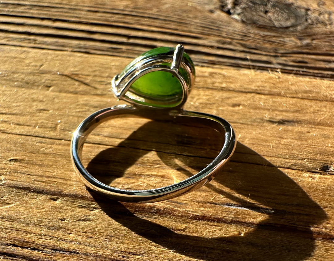 Side view of a silver ring featuring a green jade cabochon on a wooden surface