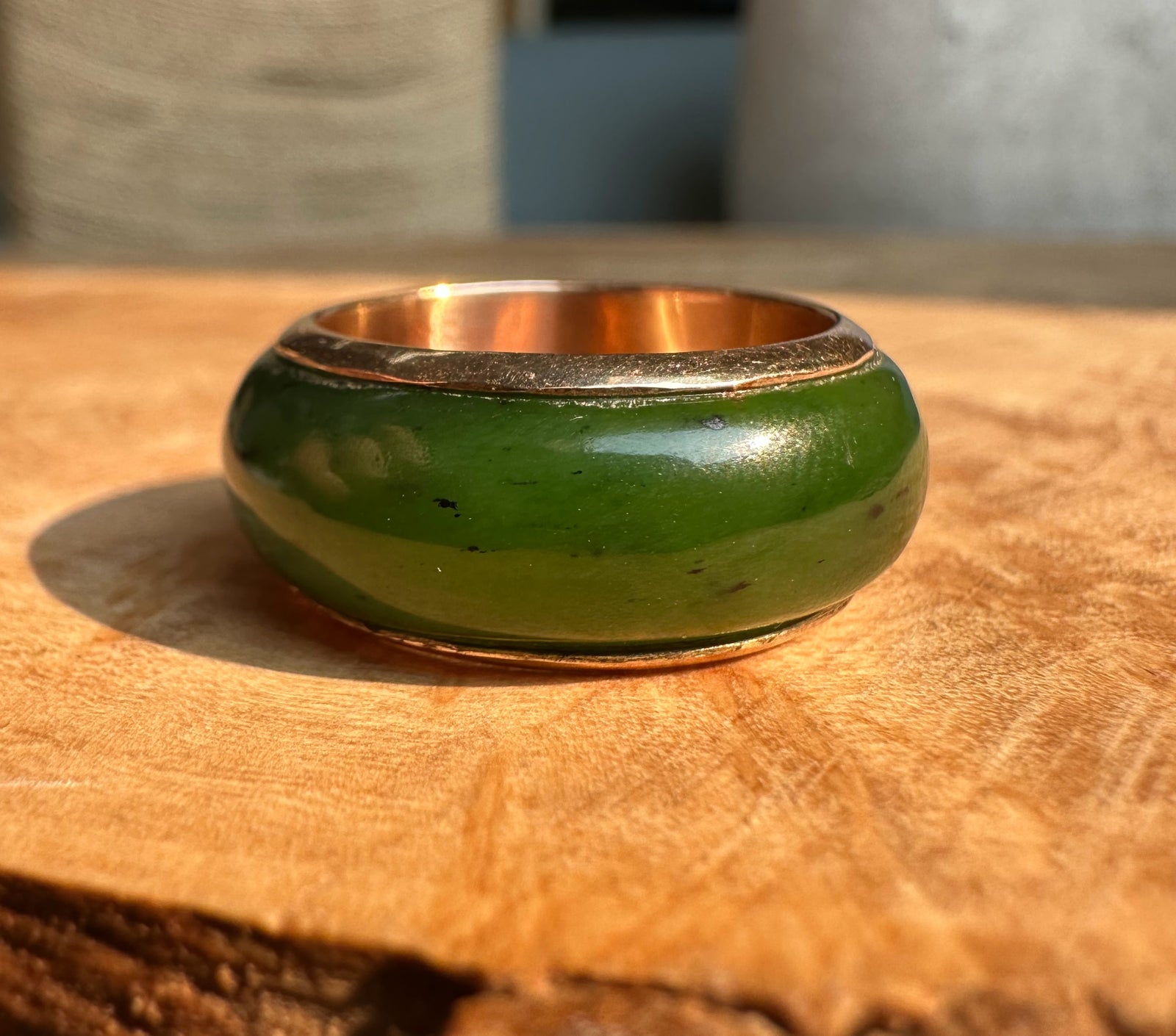 Green enamel wide band ring with gold inner edge shown from the side on a wooden surface.