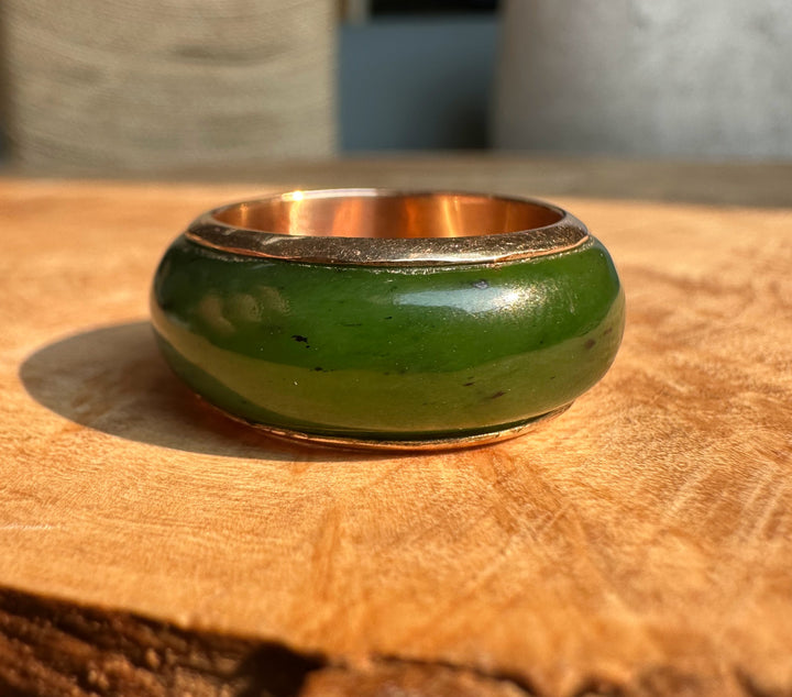 Green enamel wide band ring with gold inner edge shown from the side on a wooden surface.