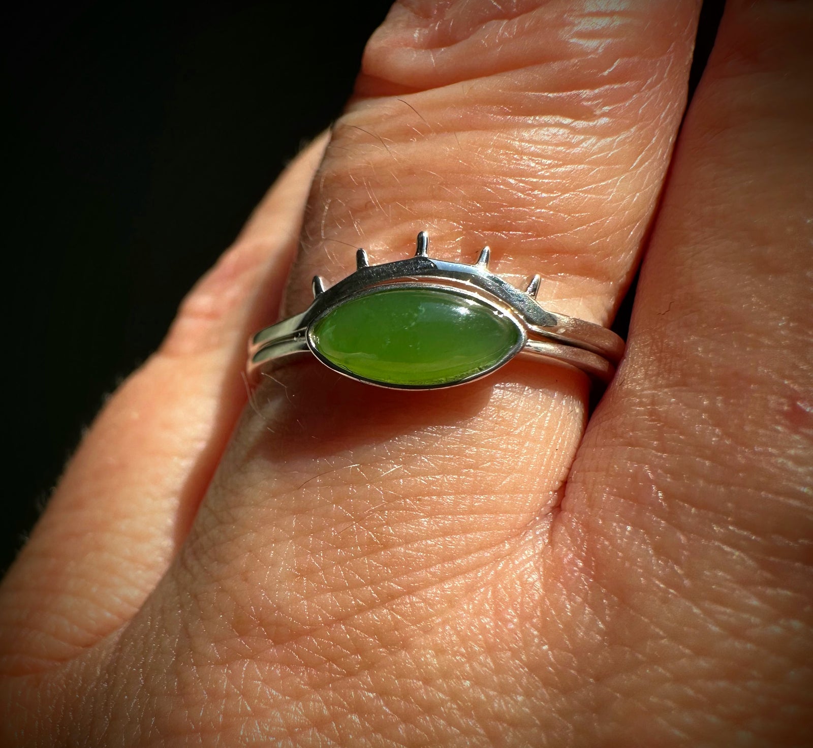 Two slim silver bands frame a bright green oval jade on a finger
