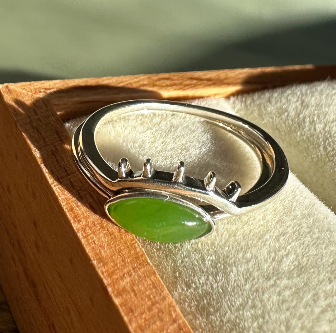 Side view of a bright green oval jade ring set in silver displayed in a wooden box