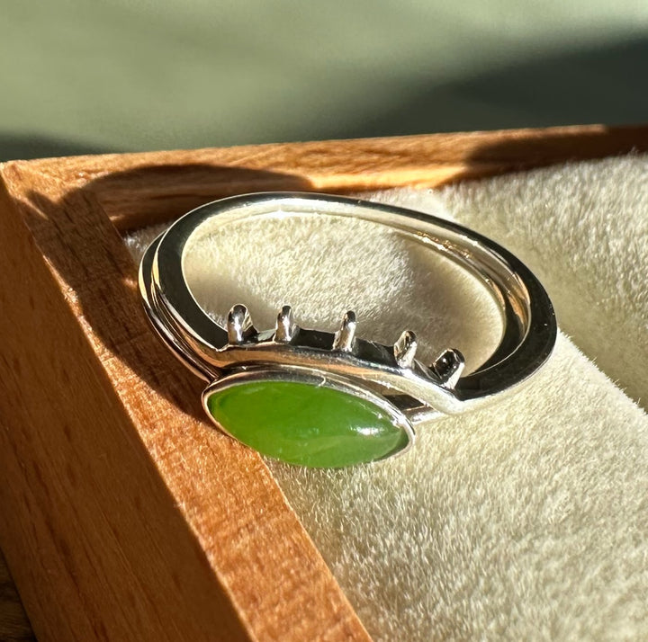 Side view of a bright green oval jade ring set in silver displayed in a wooden box