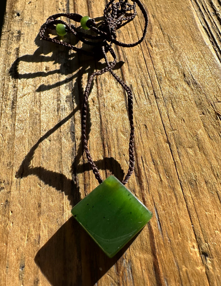 Canadian Jade Square Pendant with brown braided cord and green beads on weathered wood.