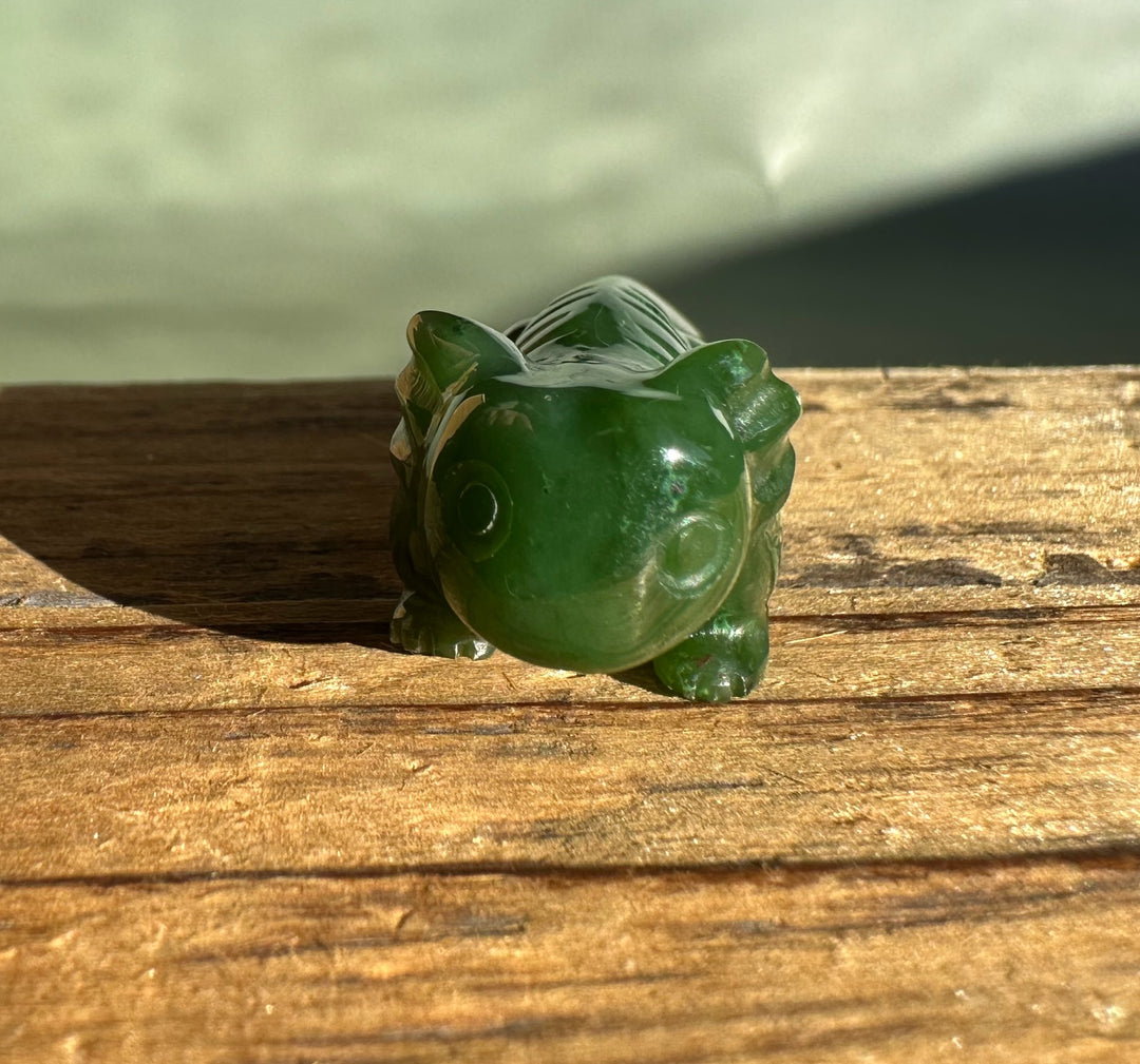 Green jade axolotl carving viewed from above on a sunlit wooden surface.