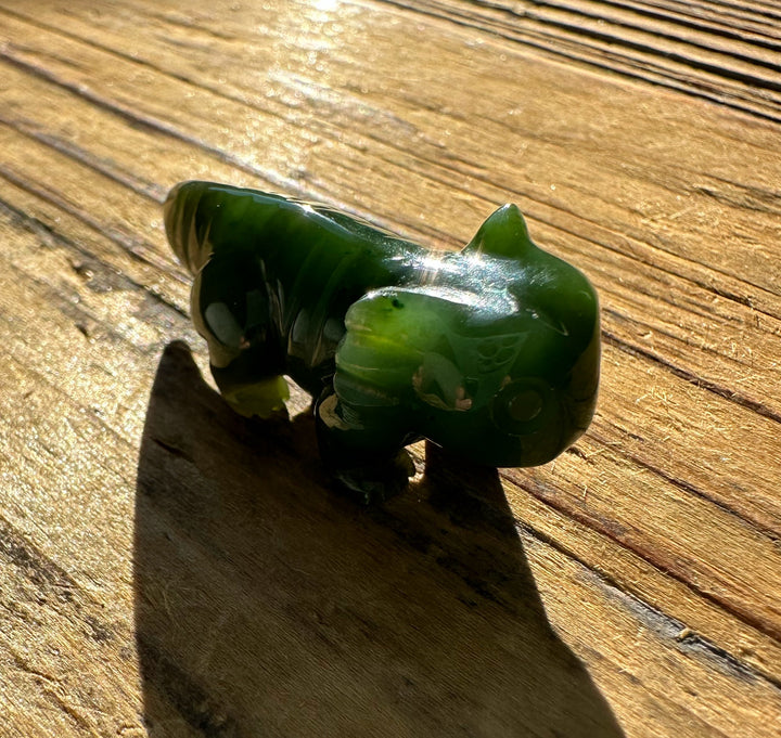 Polished Canadian jade axolotl figurine on sunlit wooden surface.