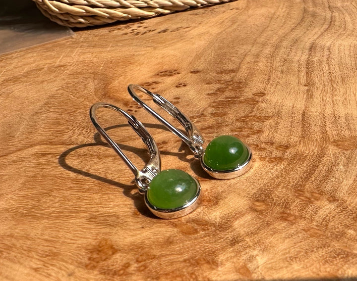 Jade round leverback earrings with silver bezels resting on a wooden surface.