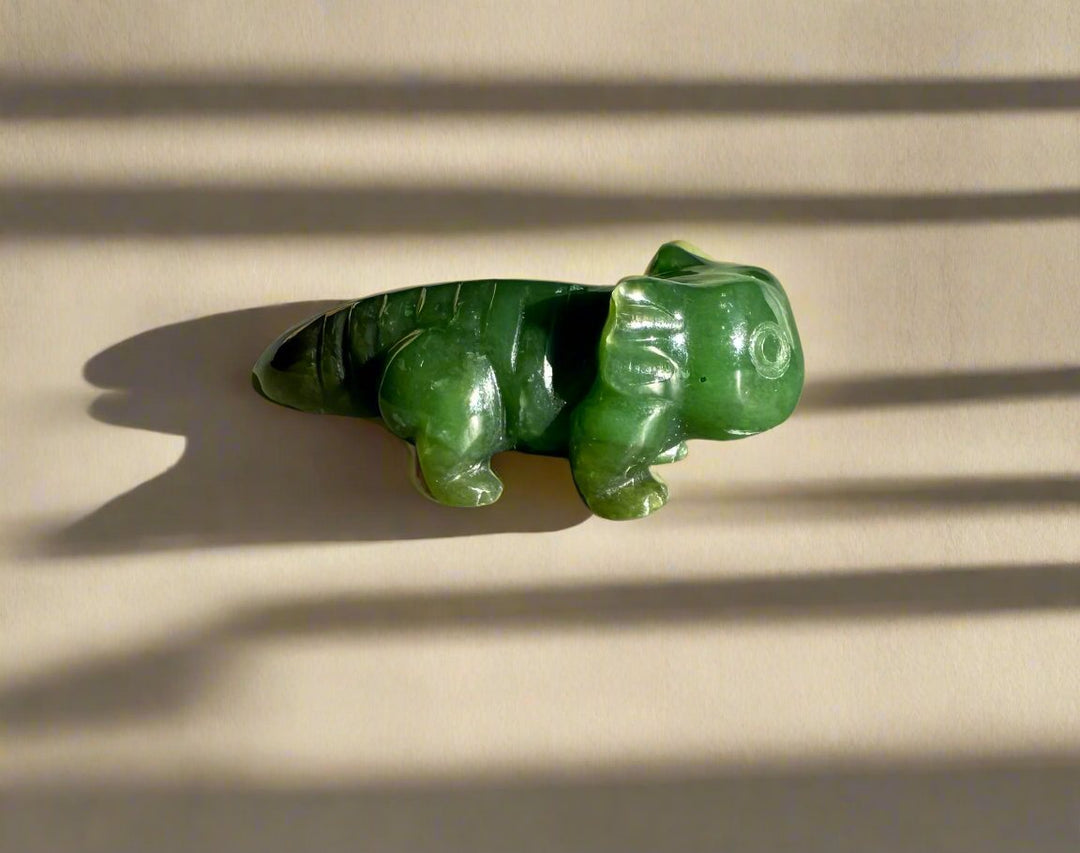 Green jade axolotl sculpture on a pale background with striped shadows.