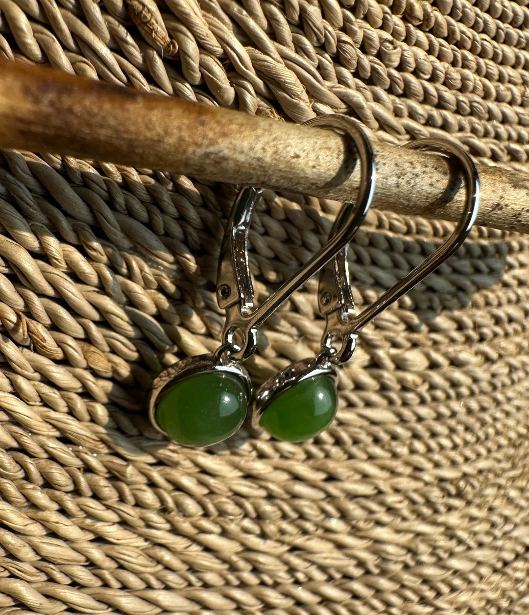 Jade round leverback earrings with silver bezels hanging from a rod against a woven background.