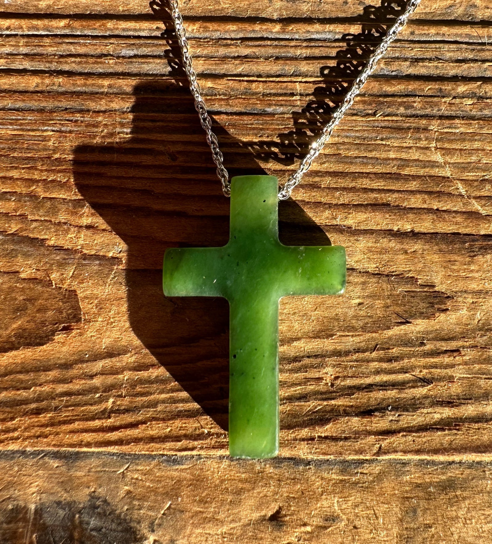 Jade cross pendant 30mm resting on wood with a silver chain draped above
