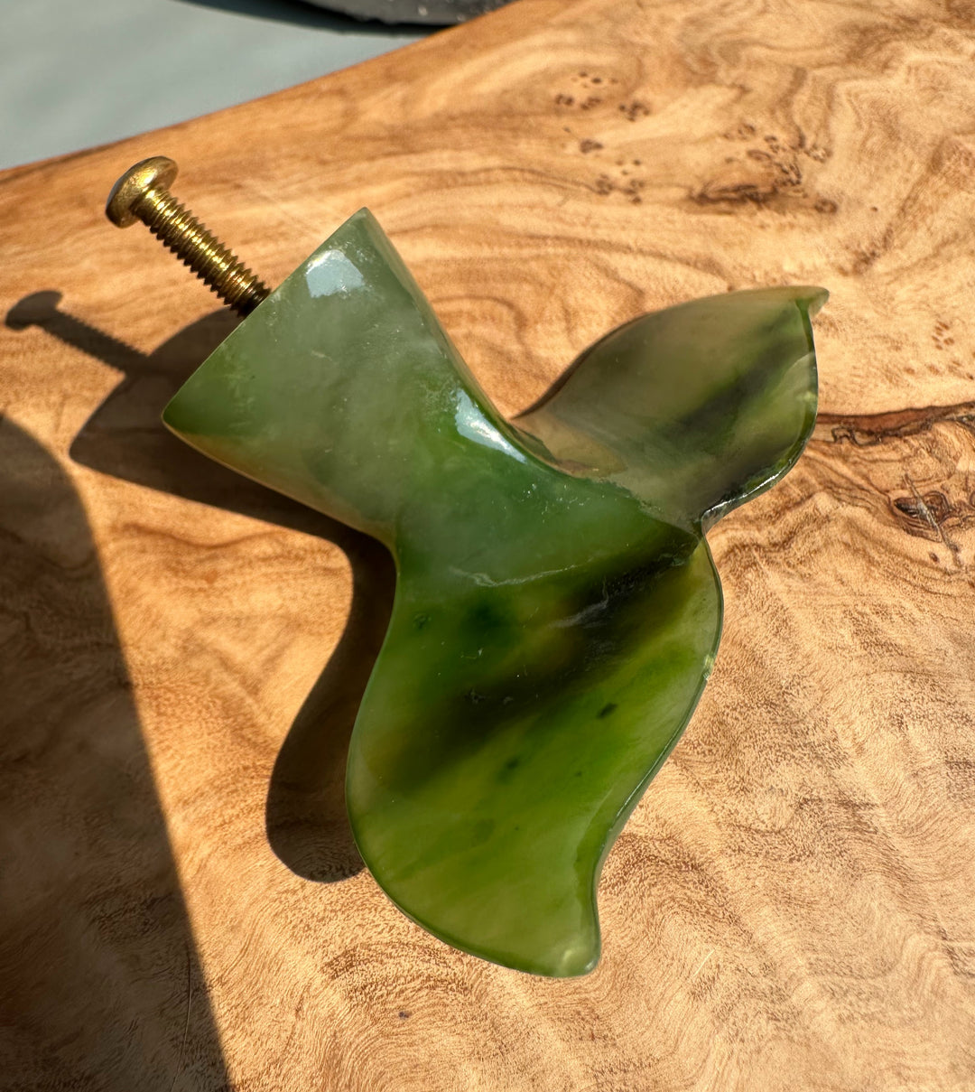 Green jade whale tail drawer pull with brass screw on a wooden surface