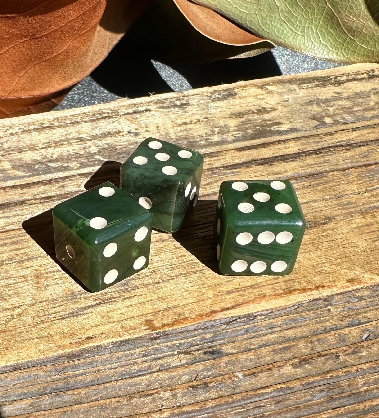 Three jade dice with white pips on a weathered wooden surface