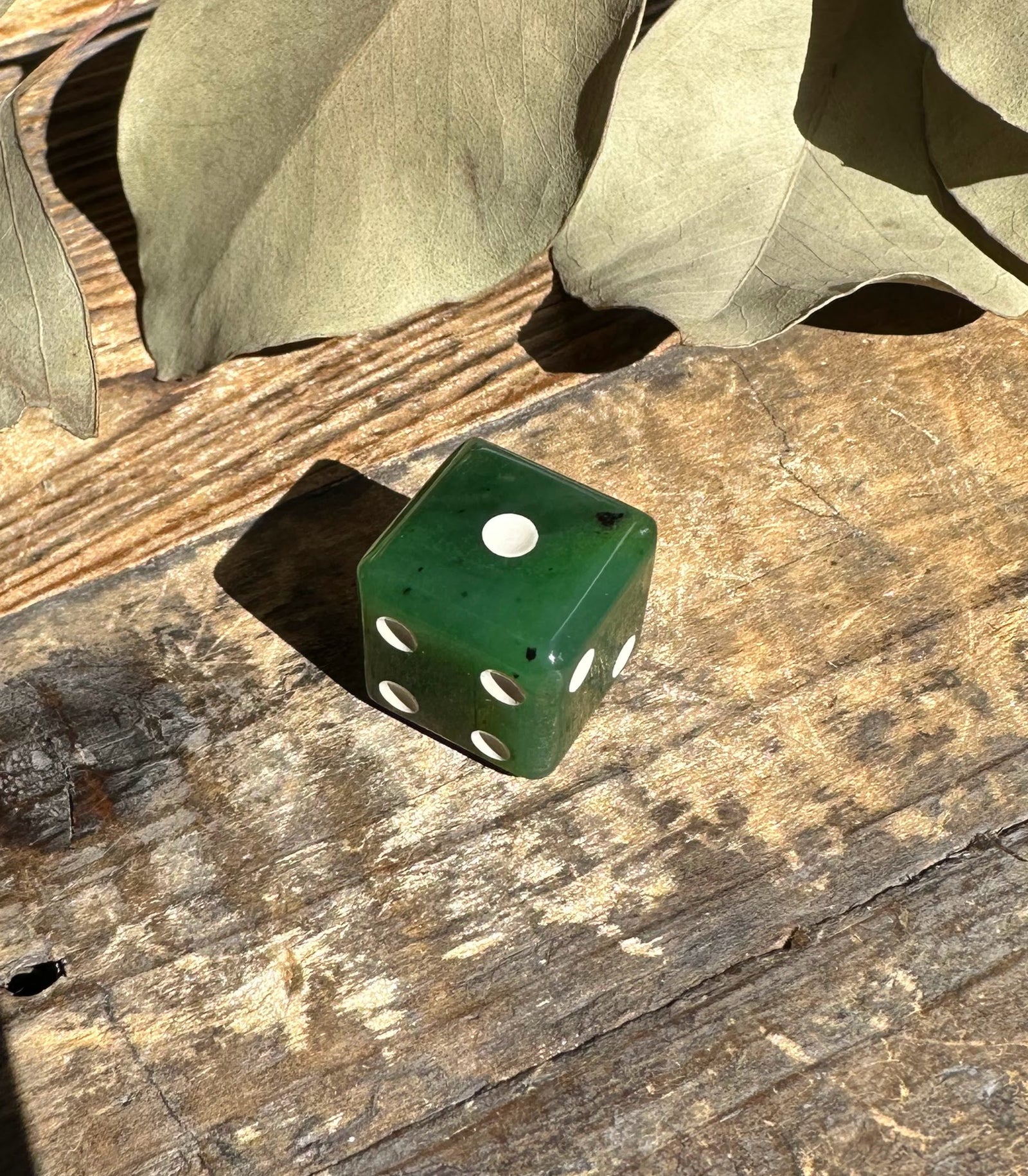 Canadian Jade 15mm die with white pips on a rustic wooden surface.