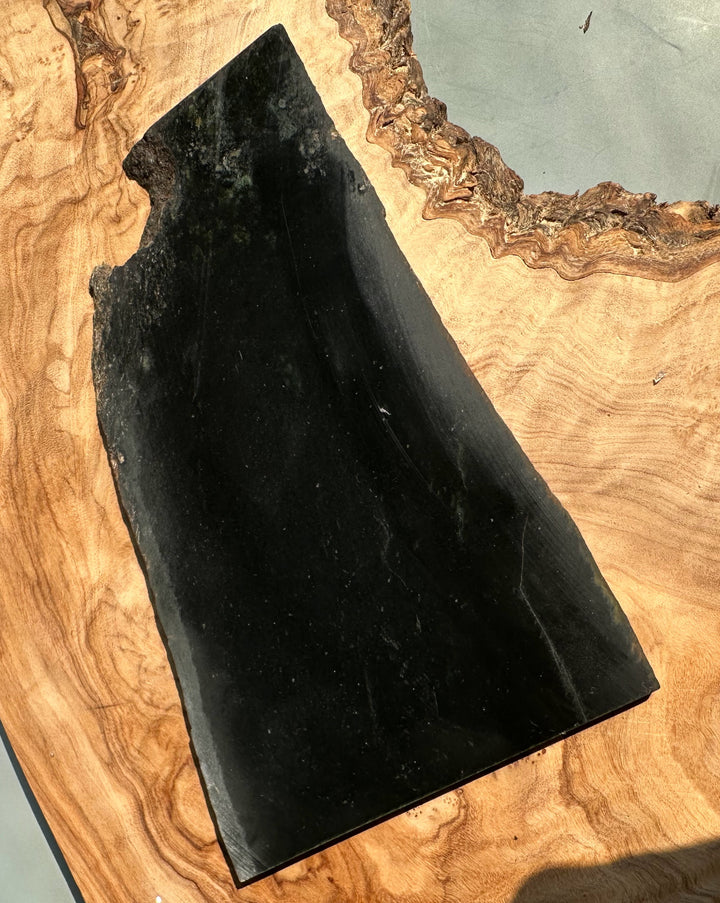Black Wyoming Jade slab with a natural rough edge resting on a wooden board.
