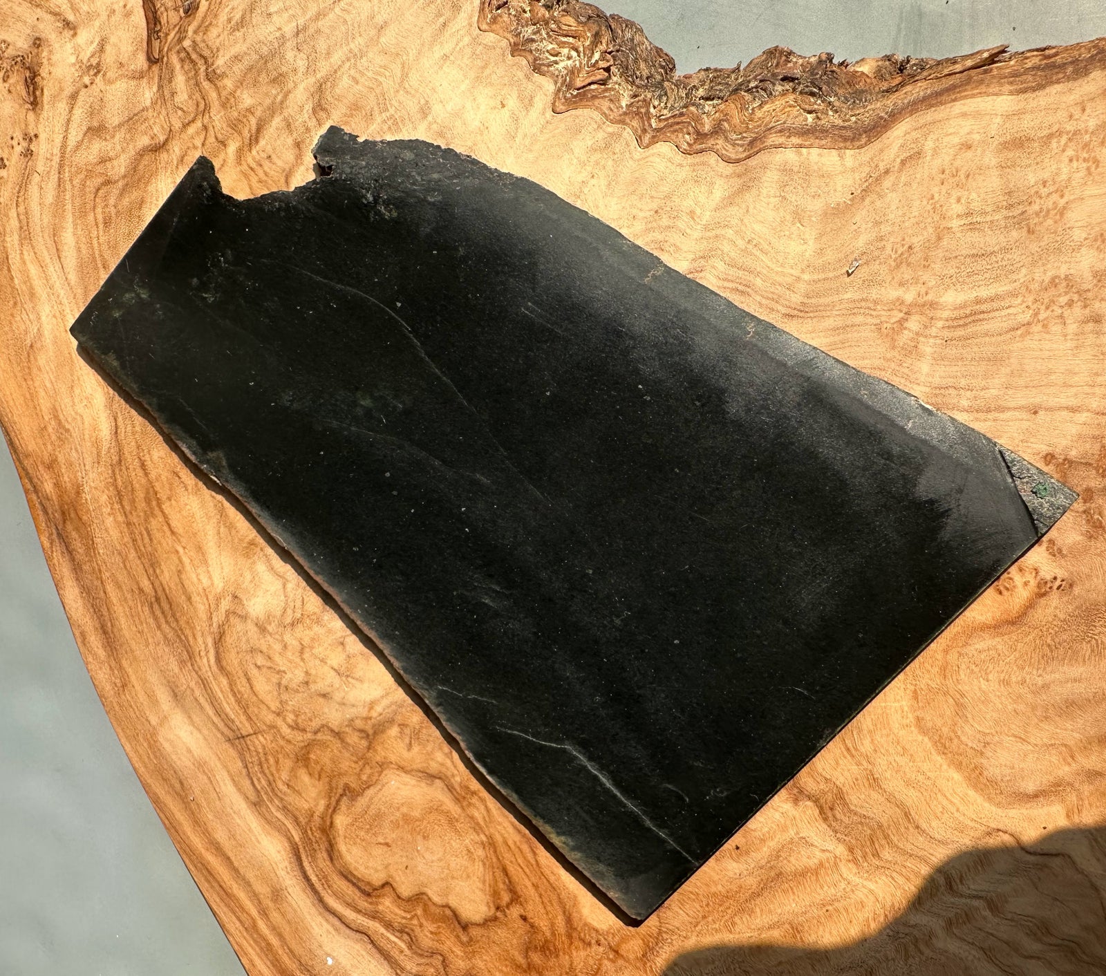 Wyoming Jade Slab black with an irregular edge resting on burl wood display board