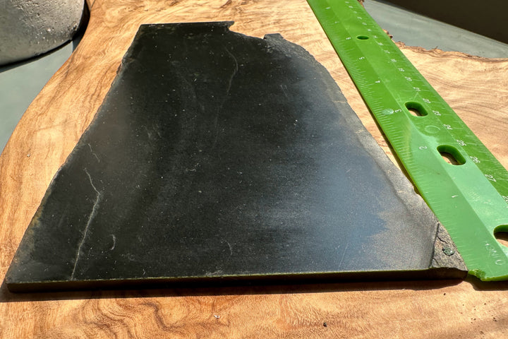 Smooth black Wyoming Jade slab on a wooden surface with a green ruler for scale.