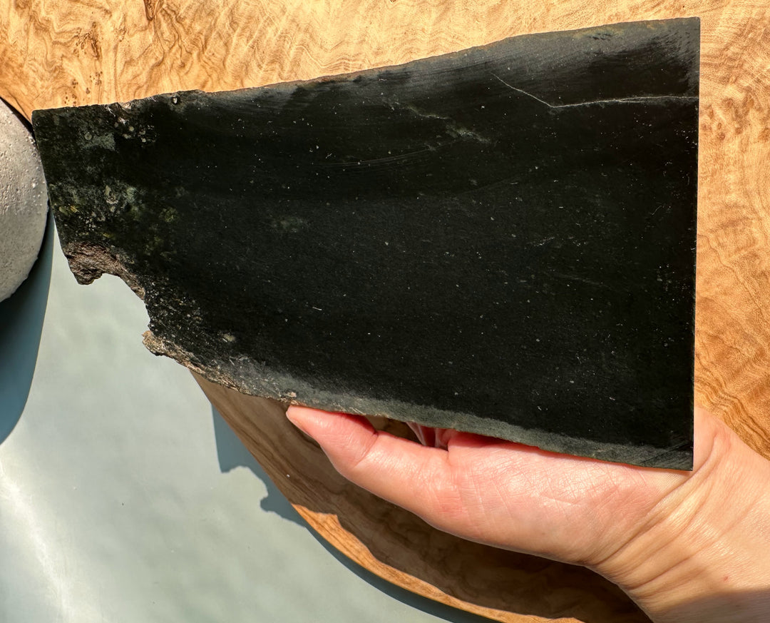 Wyoming Jade slab weighing 205 grams with a rough edge held on a wooden surface.