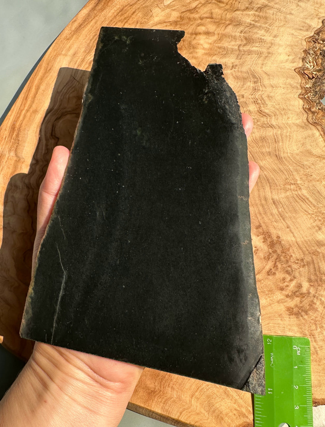 Hand holds a dark Wyoming Jade slab with a chipped top edge and rough outline.