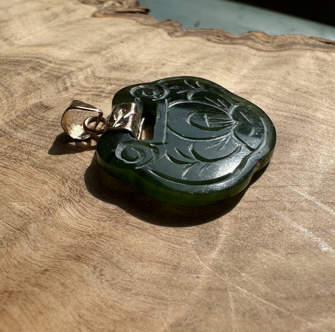 Circular dark green jade pendant carved with a blooming flower and a gold-tone bail