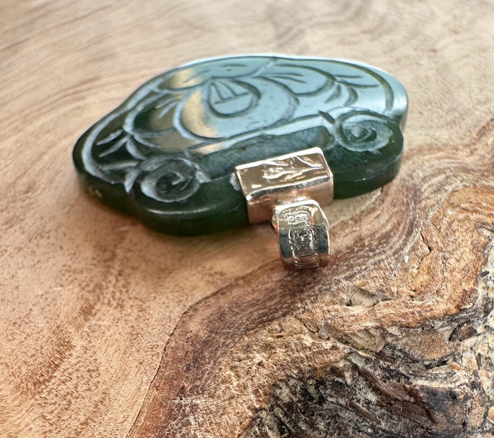 Close up of vintage jade pendant with floral carving and a silver bail on a wooden surface