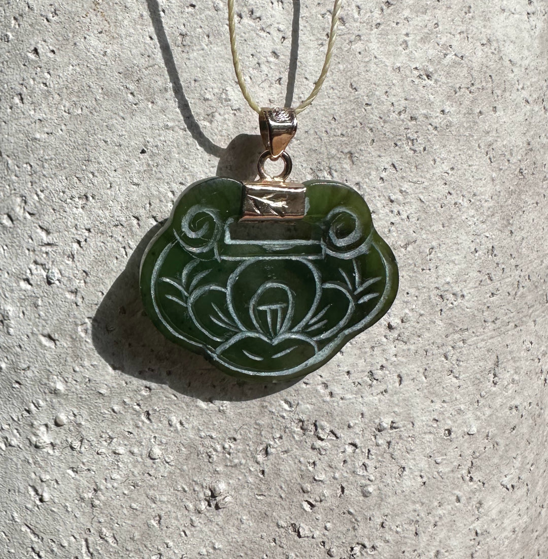 Vintage green jade pendant with a carved floral motif on a light cord and gold bail.