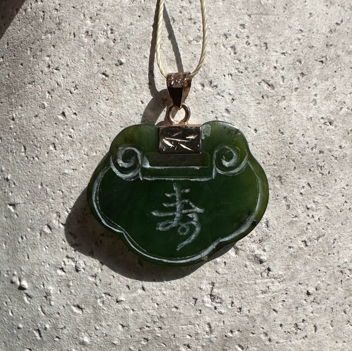 Green jade pendant shaped like a flower with a carved character, suspended from a light cord