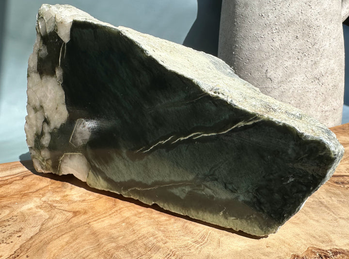 Rough Wyoming Jade piece with glossy dark green face and lighter rind on a wooden surface.