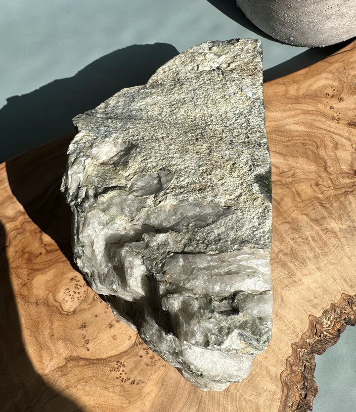 Rough Wyoming jade specimen with layered gray rock on a natural wood surface