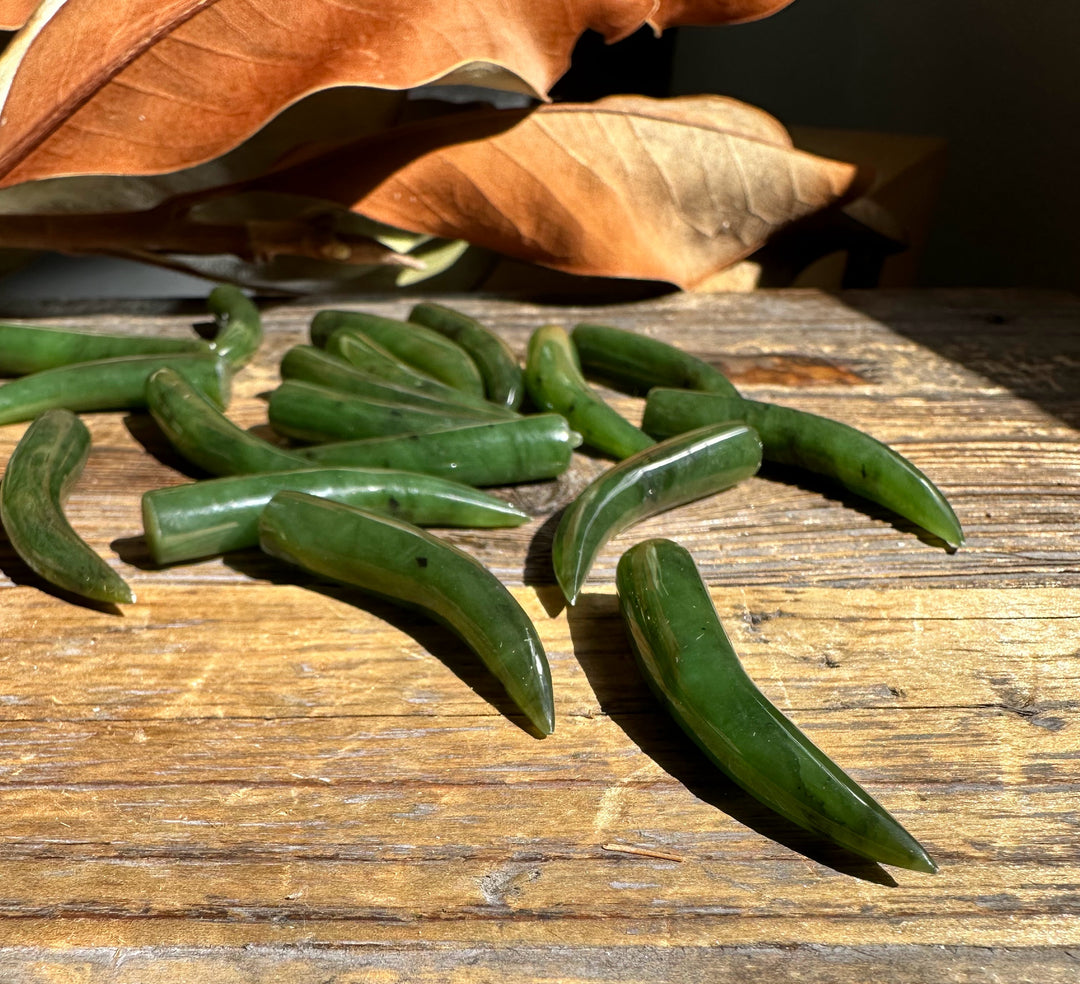 Green jade talons scattered on a weathered wooden surface with dried autumn leaves.