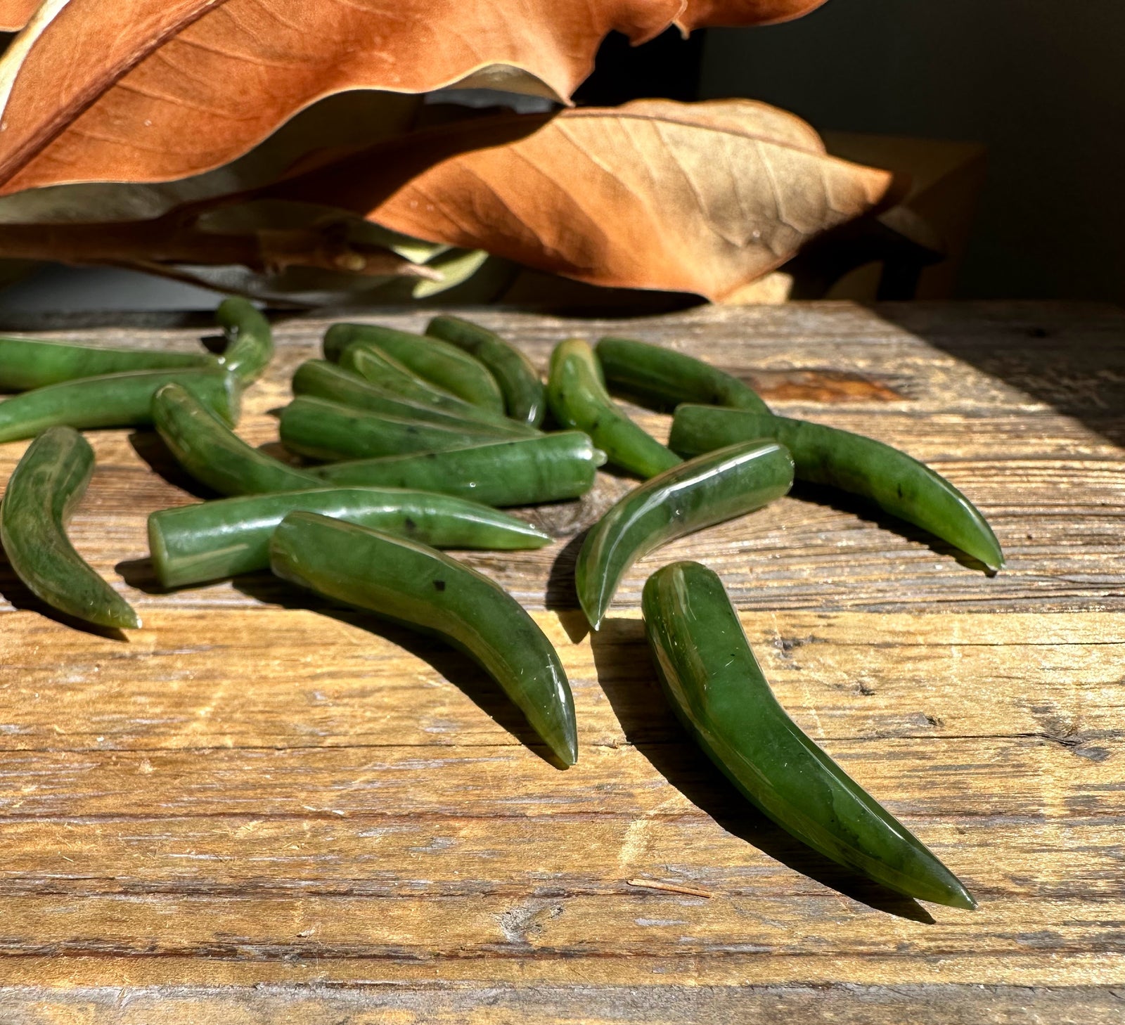 Green jade talons scattered on a weathered wooden surface with dried autumn leaves.
