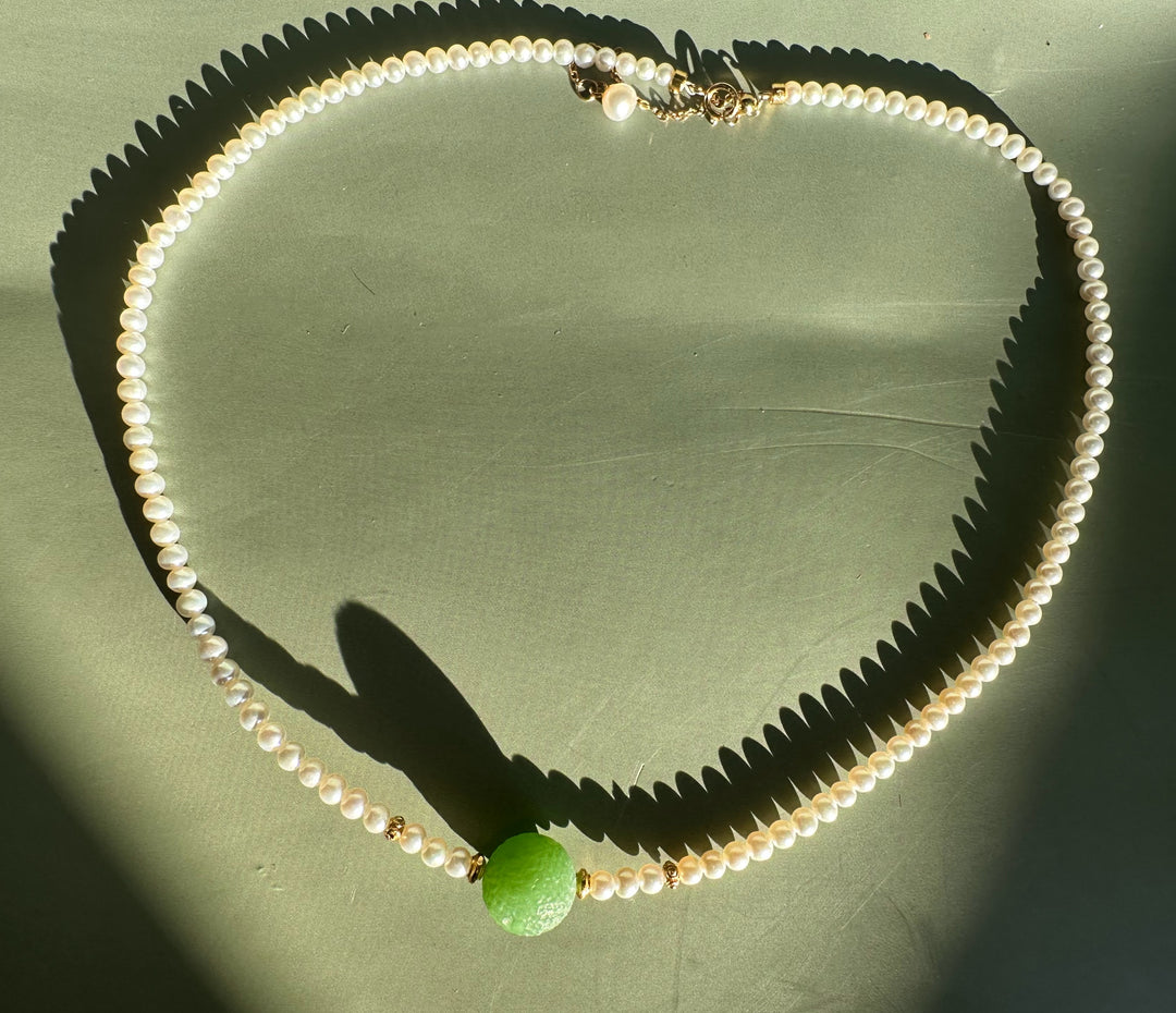 Siberian and Pearl Necklace arranged in a circle with white pearls gold spacers and a large green central bead on a green background