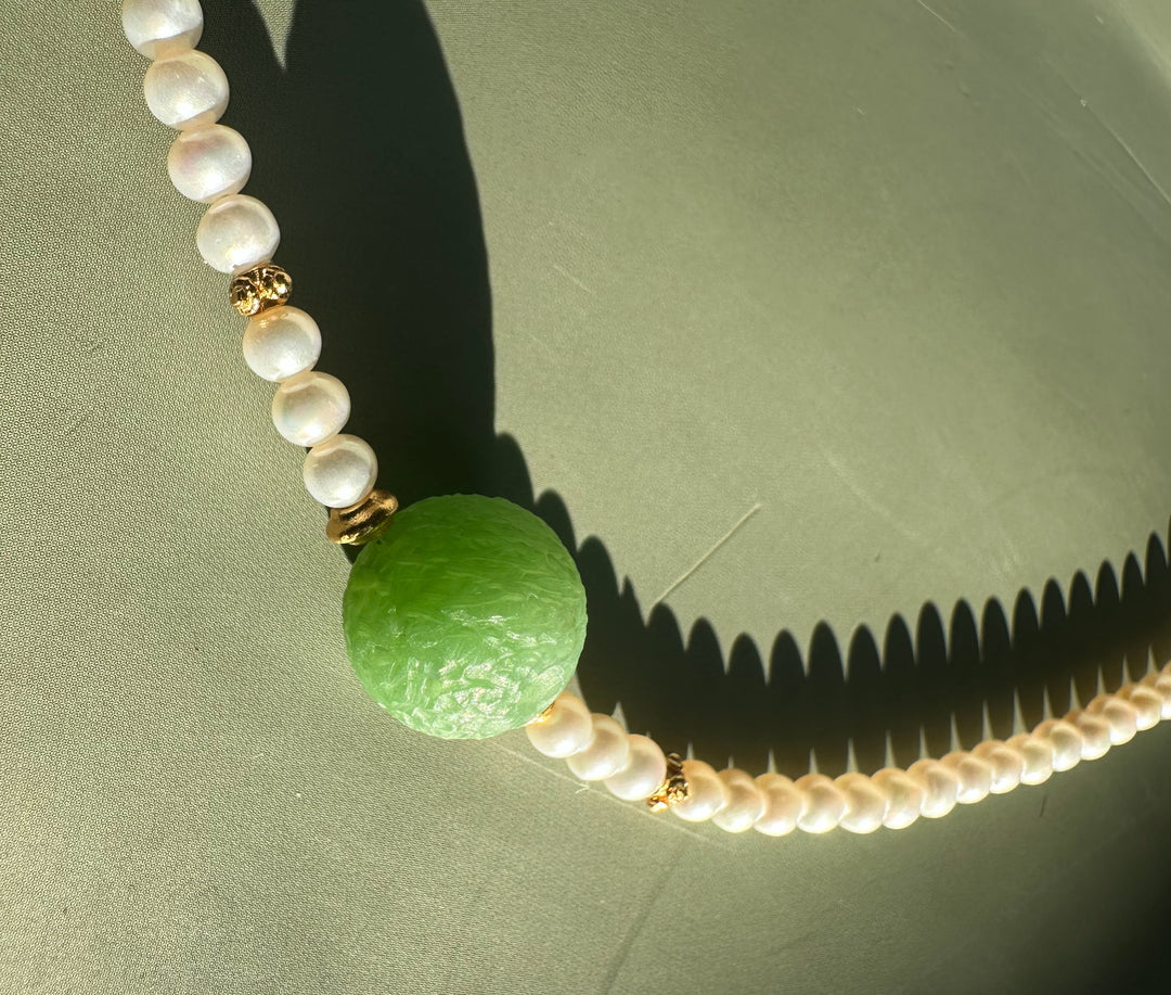 Another close view of Siberian and Pearl Necklace highlighting the green central bead and pearl strand against a green surface