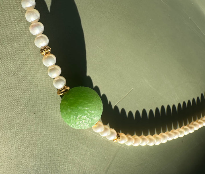 Another close view of Siberian and Pearl Necklace highlighting the green central bead and pearl strand against a green surface