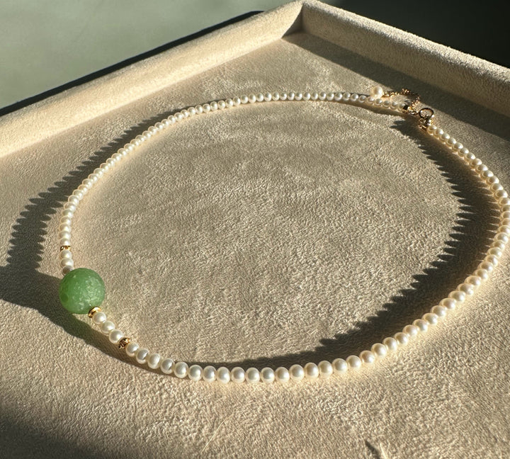 Siberian and Pearl Necklace laid out on a beige display tray showing a green centerpiece bead and gold spacers.