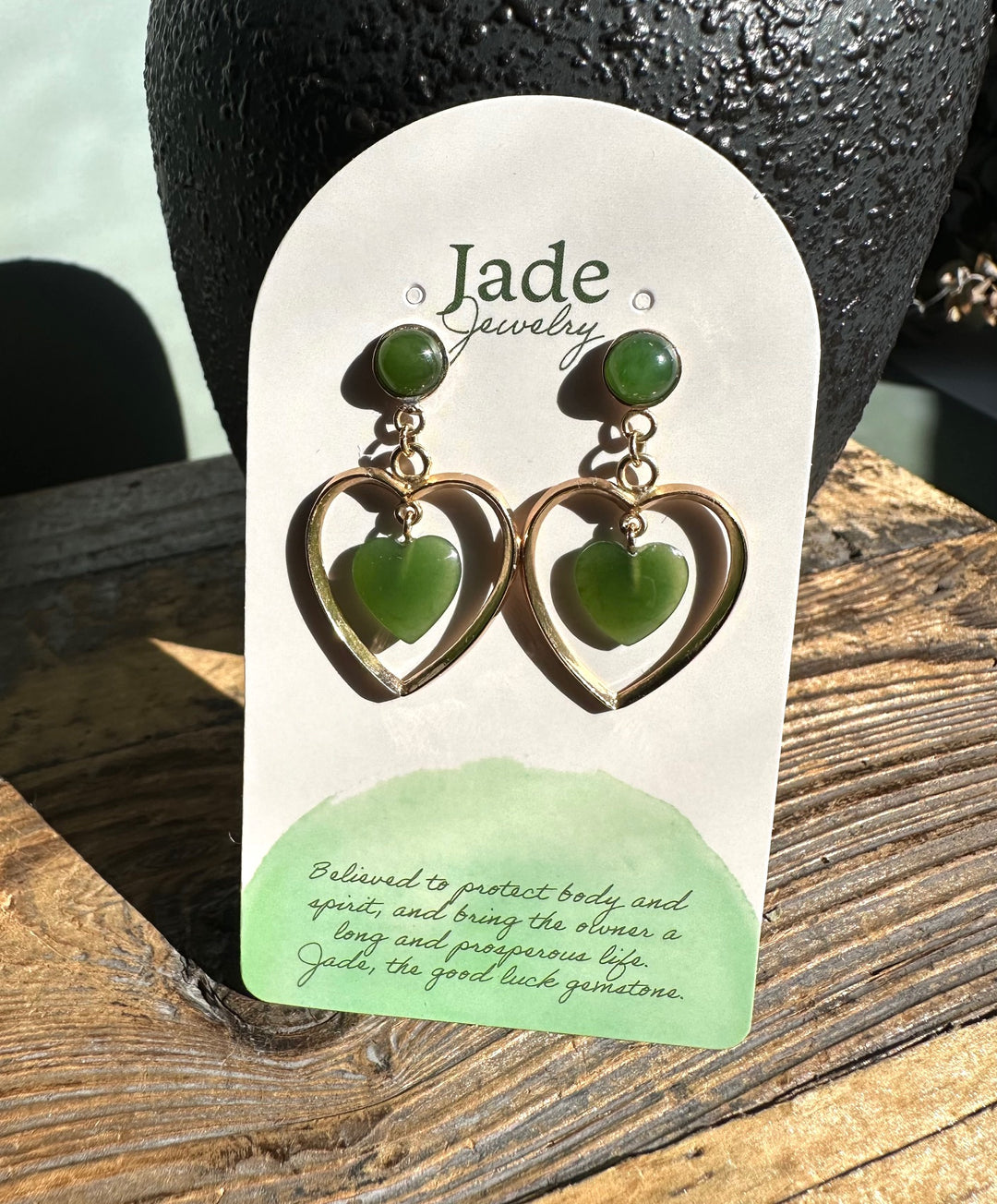 Green jade heart earrings with gold open heart frames hanging on a Jade Jewelry display card