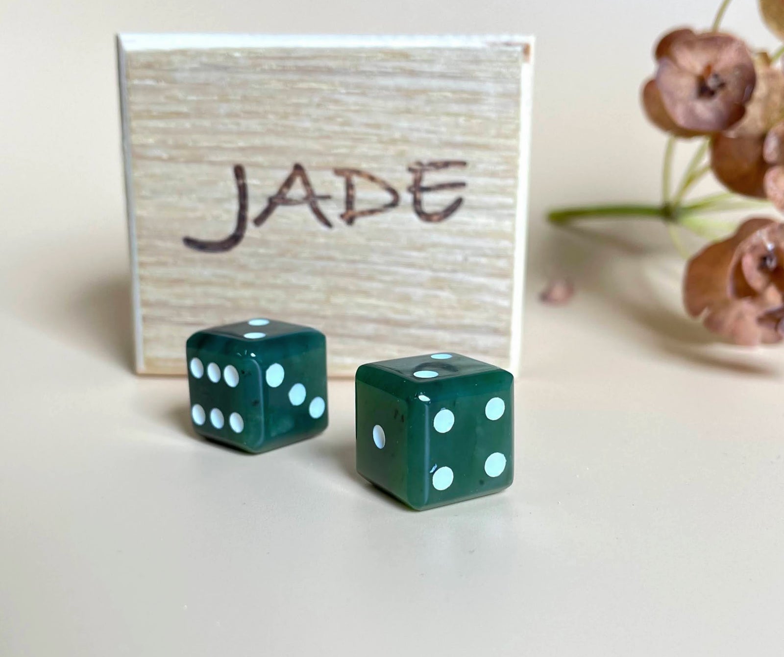 Two green dice with white pips in front of a light wooden Jade gift box