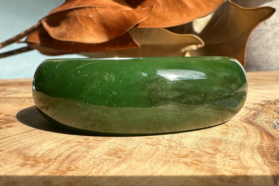 A+ Canadian Jade Oval Bangle 52.5mm green jade on wood surface with curved glossy edge