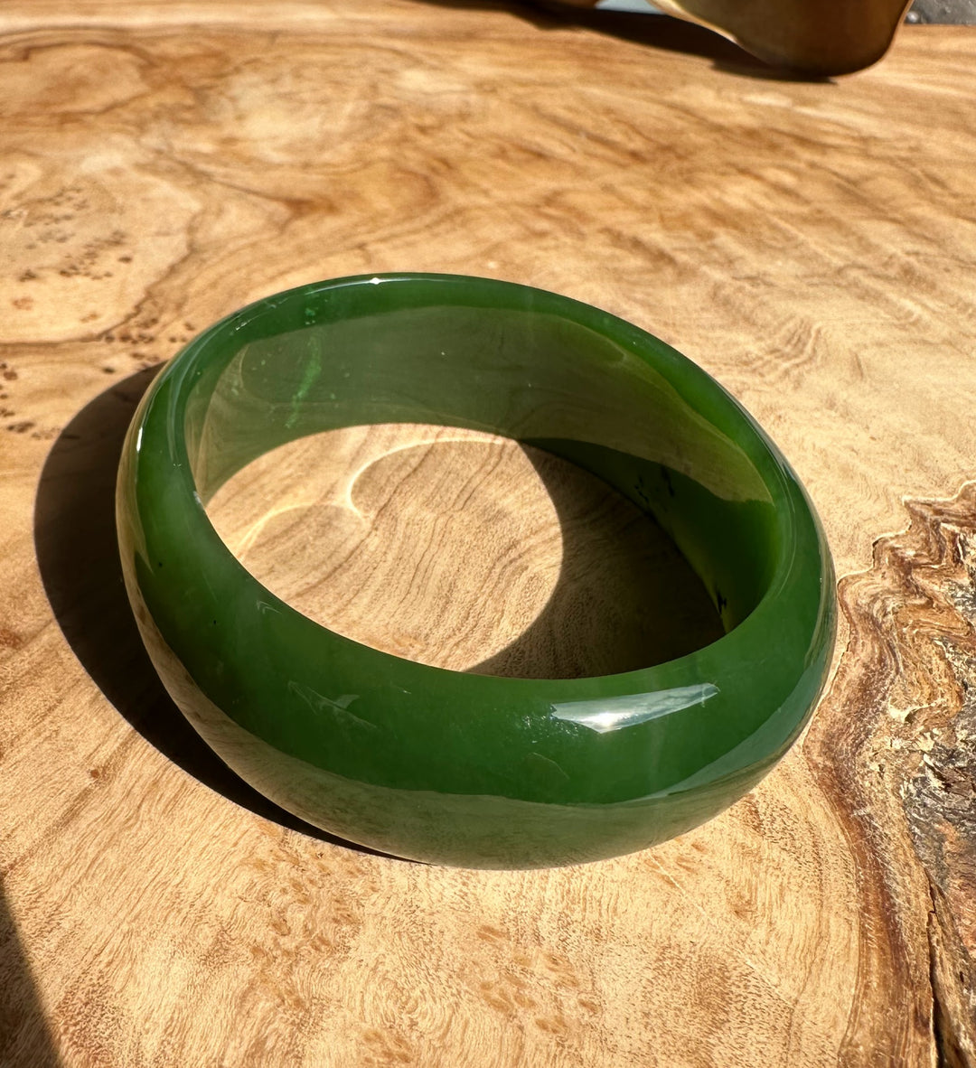 A+ Canadian Jade Oval Bangle 52.5mm in vibrant green on a wooden tabletop with a polished glossy finish.