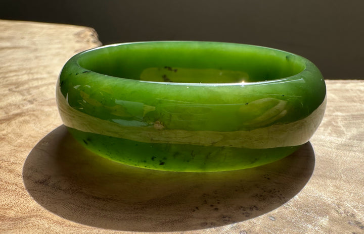Vivid green Canadian jade oval bangle 52.5mm resting on a wooden surface