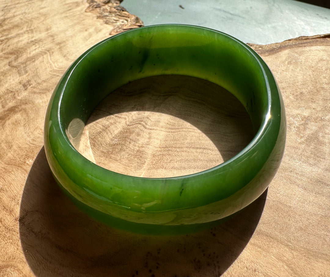 Bright green jade oval bangle with a smooth polished surface resting on a wooden surface