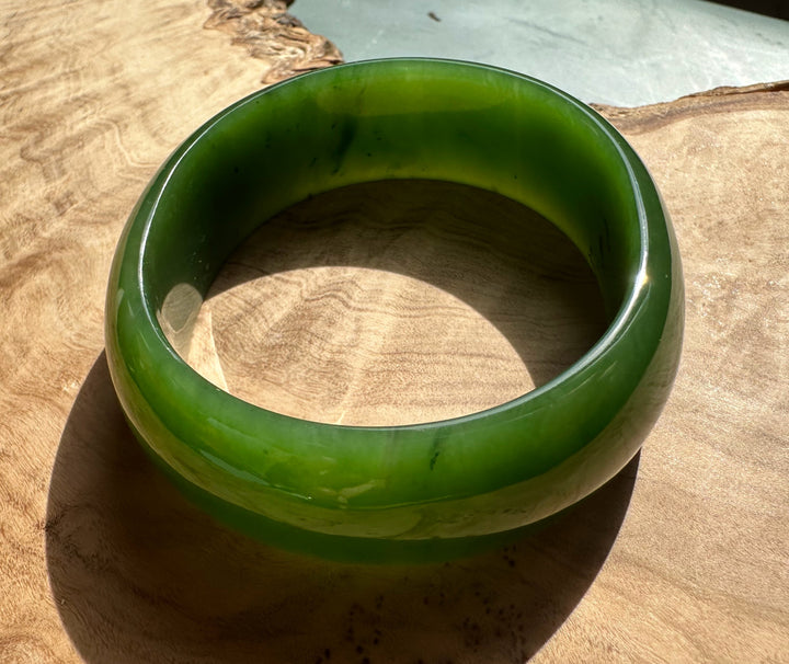 Bright green jade oval bangle with a smooth polished surface resting on a wooden surface