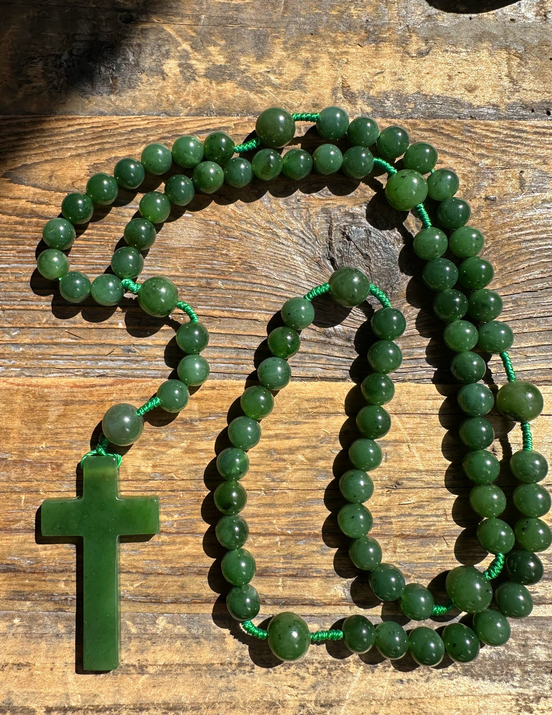 Jade bead rosary with green cross pendant on a weathered wooden surface