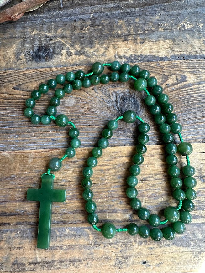 Close up of jade bead rosary with green cross pendant on a wooden surface