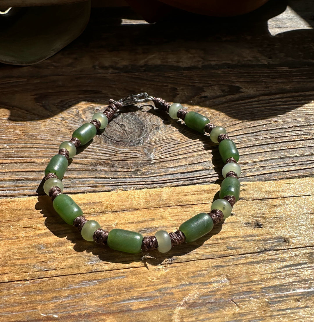 Bracelet 2243-2 with green jade beads and brown braided cord on a rustic wooden surface