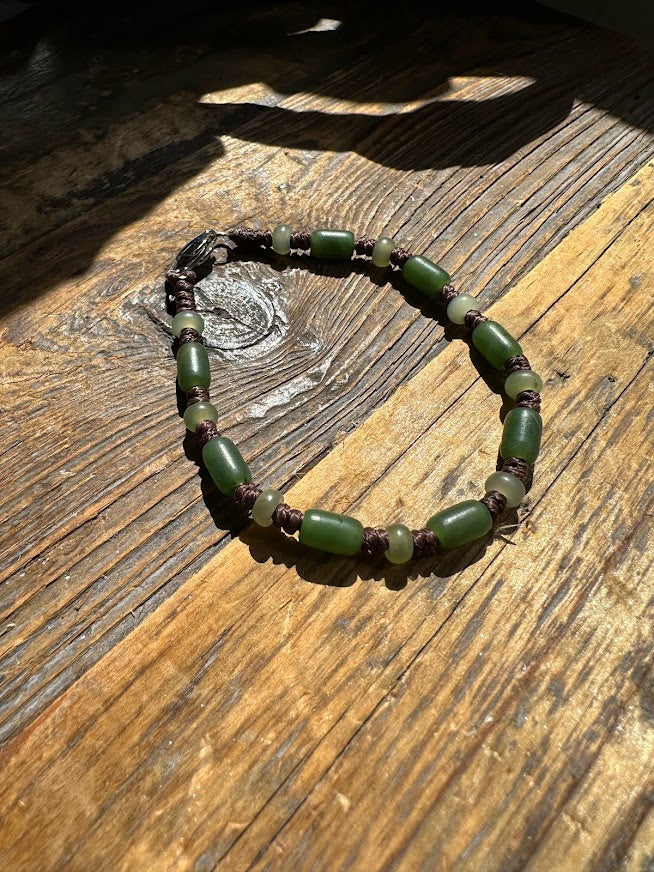 Bracelet with green cylindrical beads and small pale green rounds laid on weathered wooden surface.