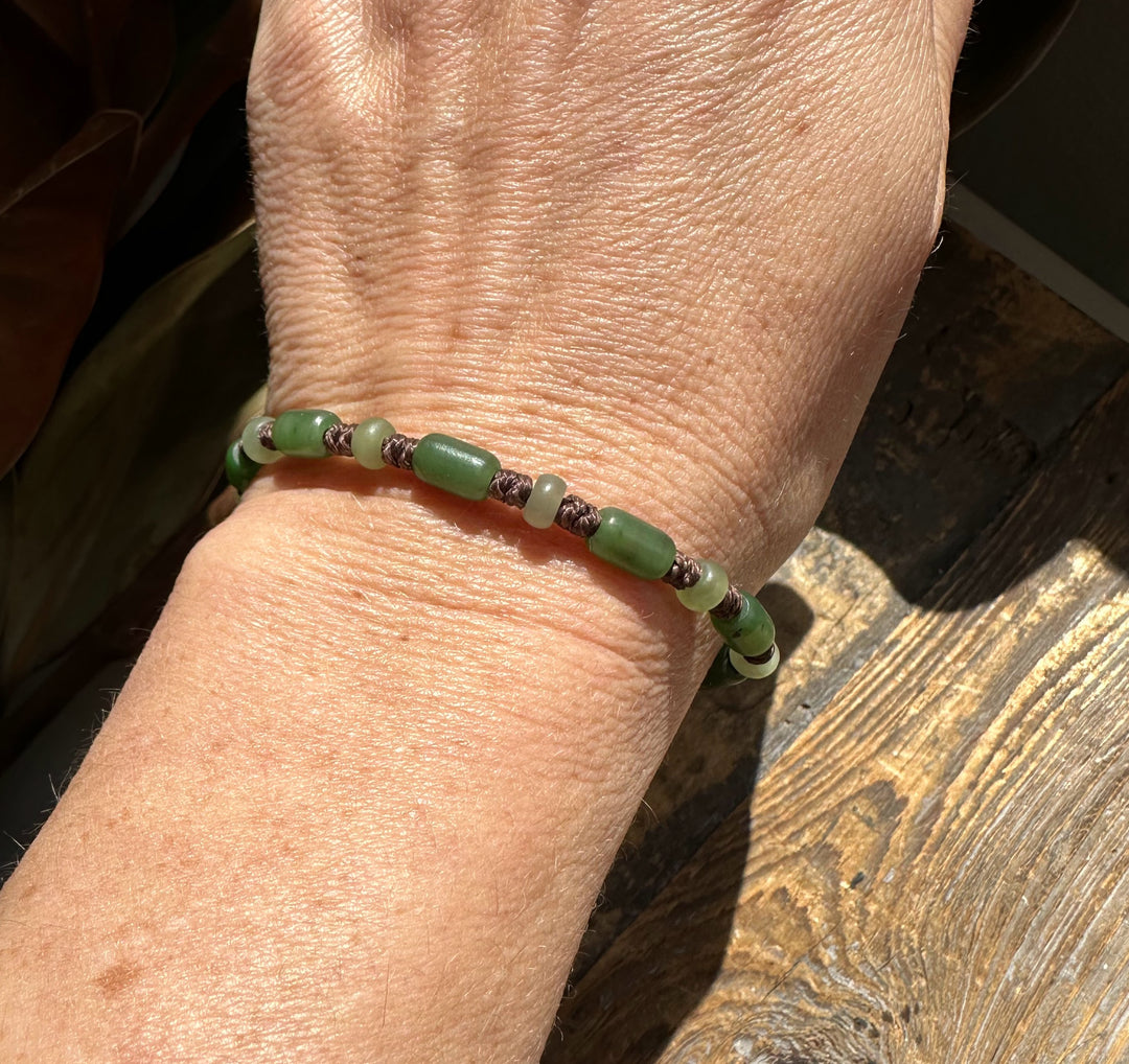 Close up of the beaded bracelet on the wrist with alternating green cylinders and light green rounds tied by dark brown cord.