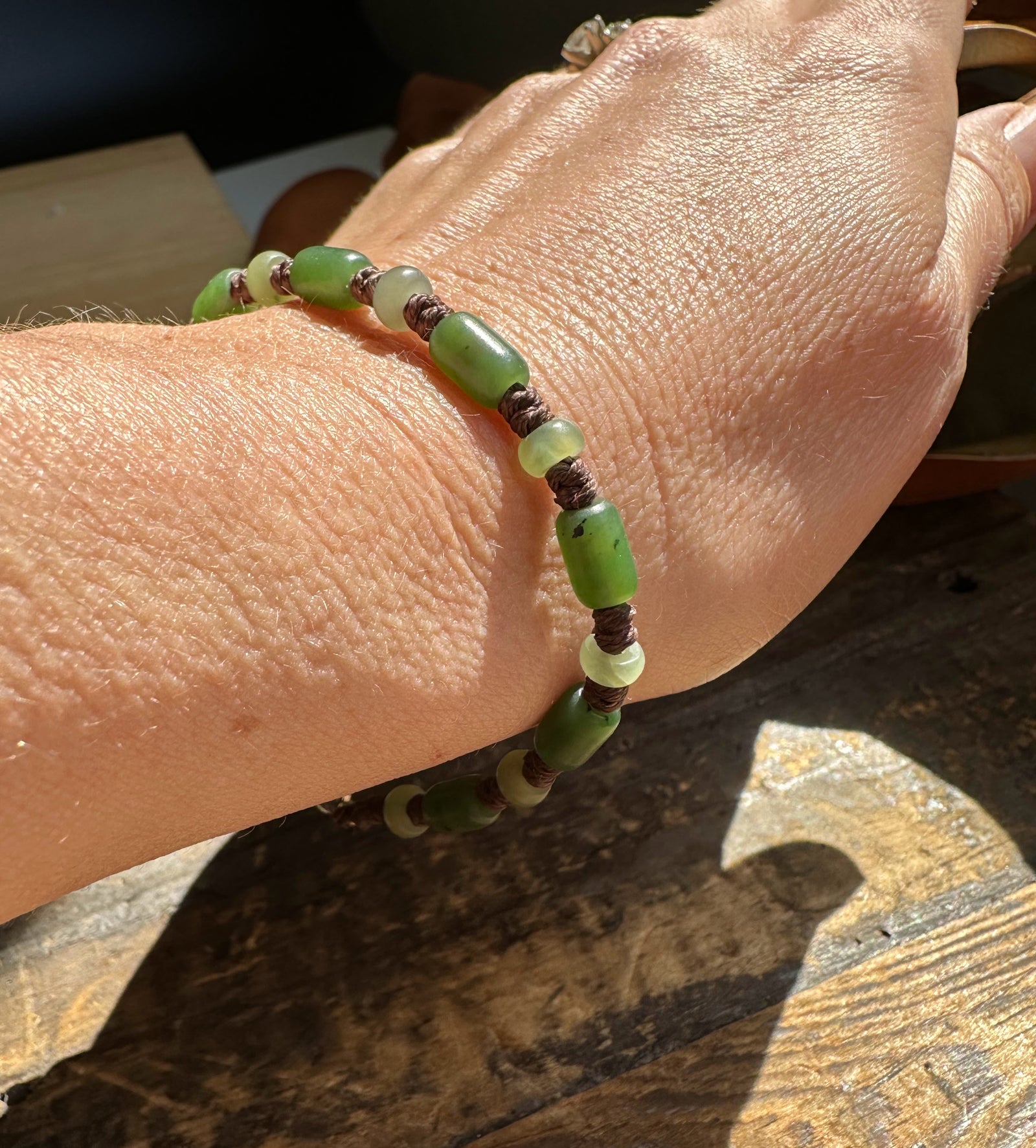 Wrist shot showing green cylindrical beads and pale rounds separated by brown knotted cord.