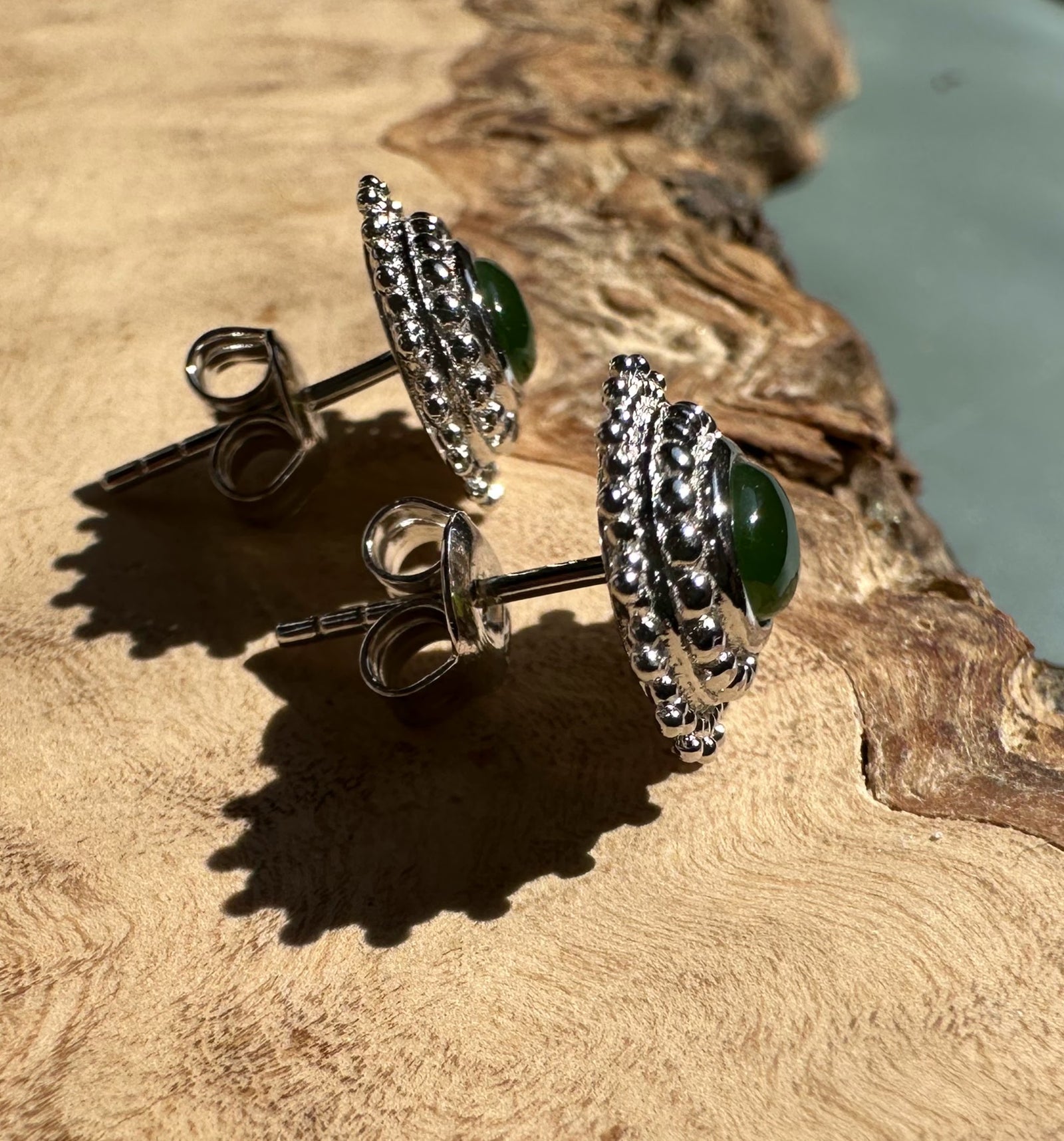 Canadian Jade and Silver Earrings with oval green jade centerpiece and beaded silver halo on a wood surface