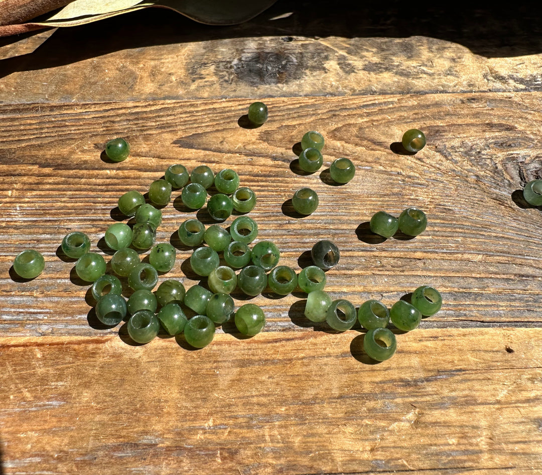 Loose group of 6mm Canadian Jade beads with large holes spread across a wooden surface